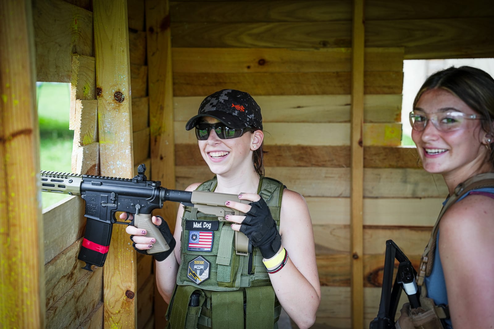 Mad Dog and a teammate smiling with airsoft markers inside a wooden structure at Coyote Field